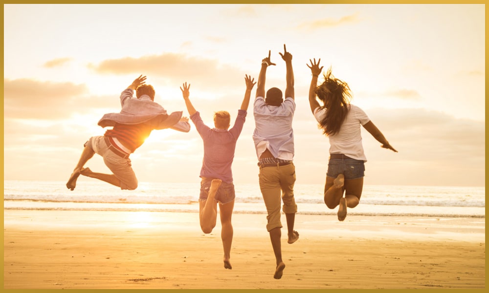 Happy group full of vitality jumping on the beach in the sand in sunshine