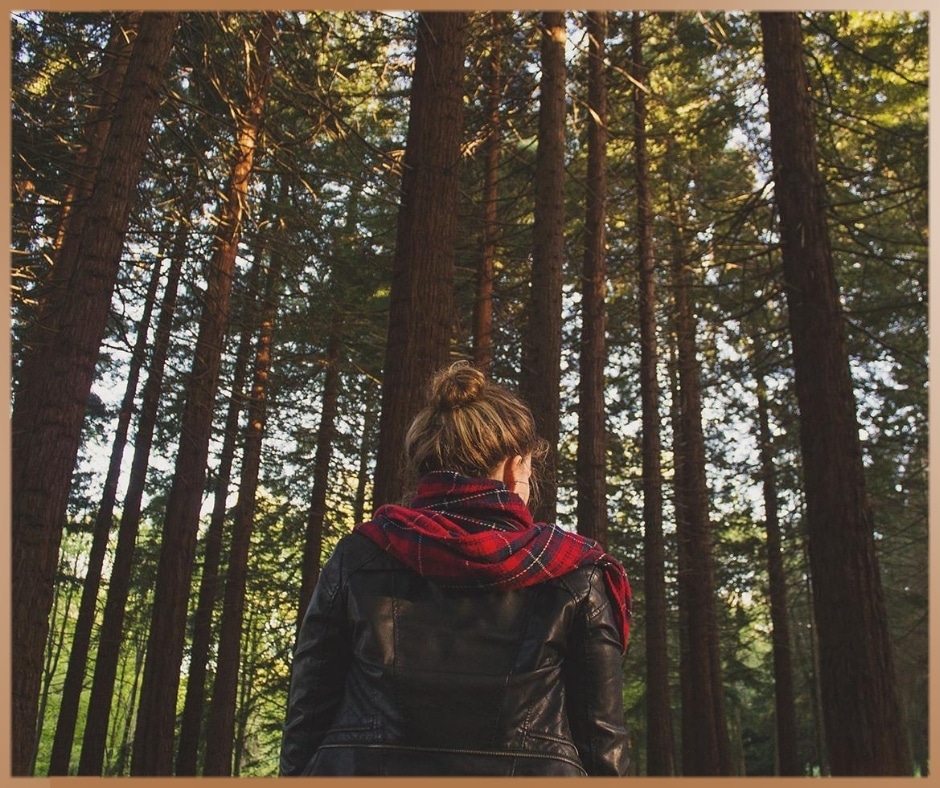 Woman in a forest is watching the trees in a scarf and leather jacket