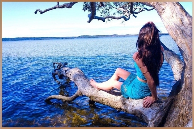 Happy woman watching a blue lake on a tree