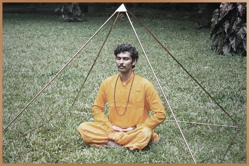 Man practices pyramid meditation under a pyramid shaped structure