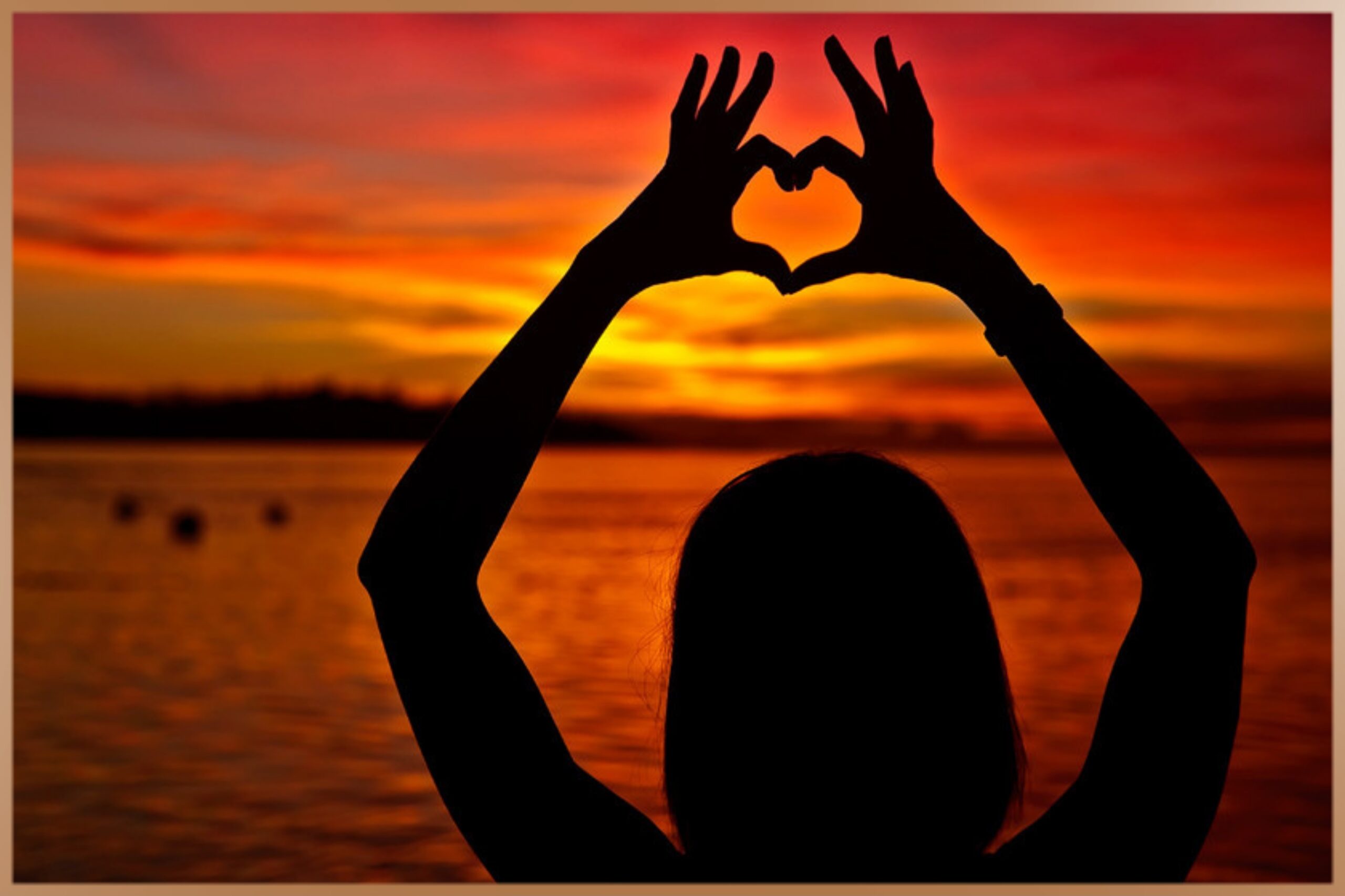 Woman shows heart with her hands during sunset at the beach