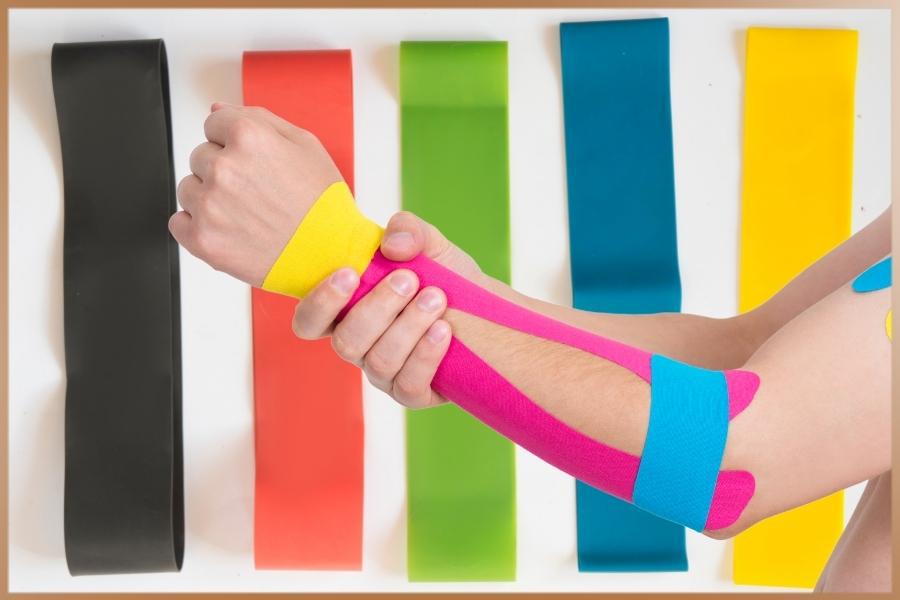 Kinesiology tapes in different colours, and a woman's arm with pink, blue and yellow tape