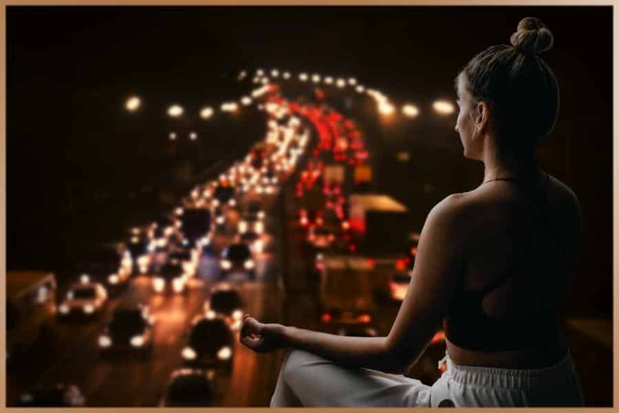 Woman meditating in background with busy road, cars in the rushing world