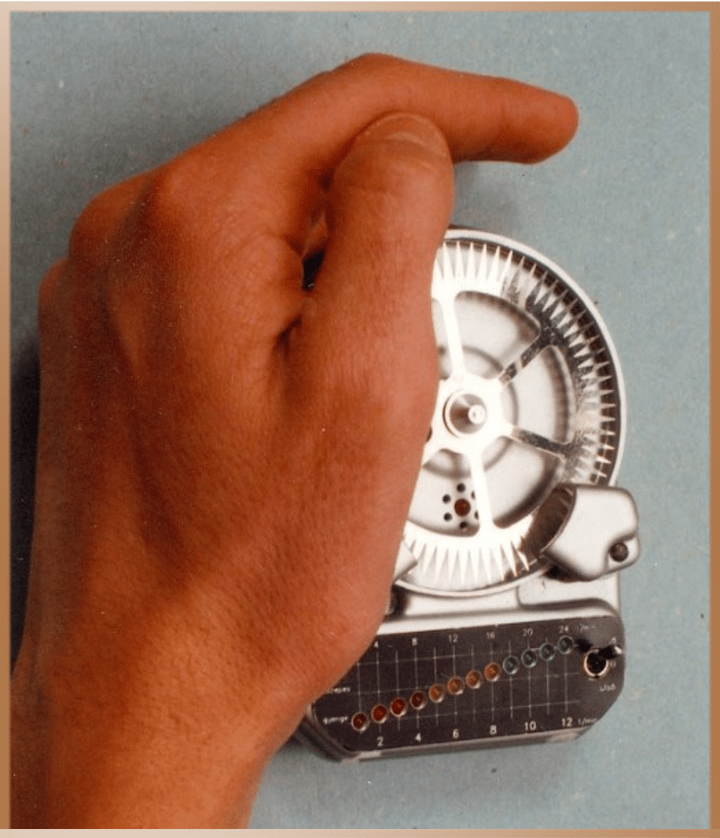 An old prototype of the Egely Wheel under a human hand, demonstrating the measurement of bioenergy through the rotation of the wheel.