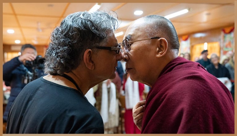 Deepak Chopra and His Holiness the Dalai Lama engage in a traditional Maori greeting by rubbing noses, symbolizing the sharing of breath and spiritual connection.