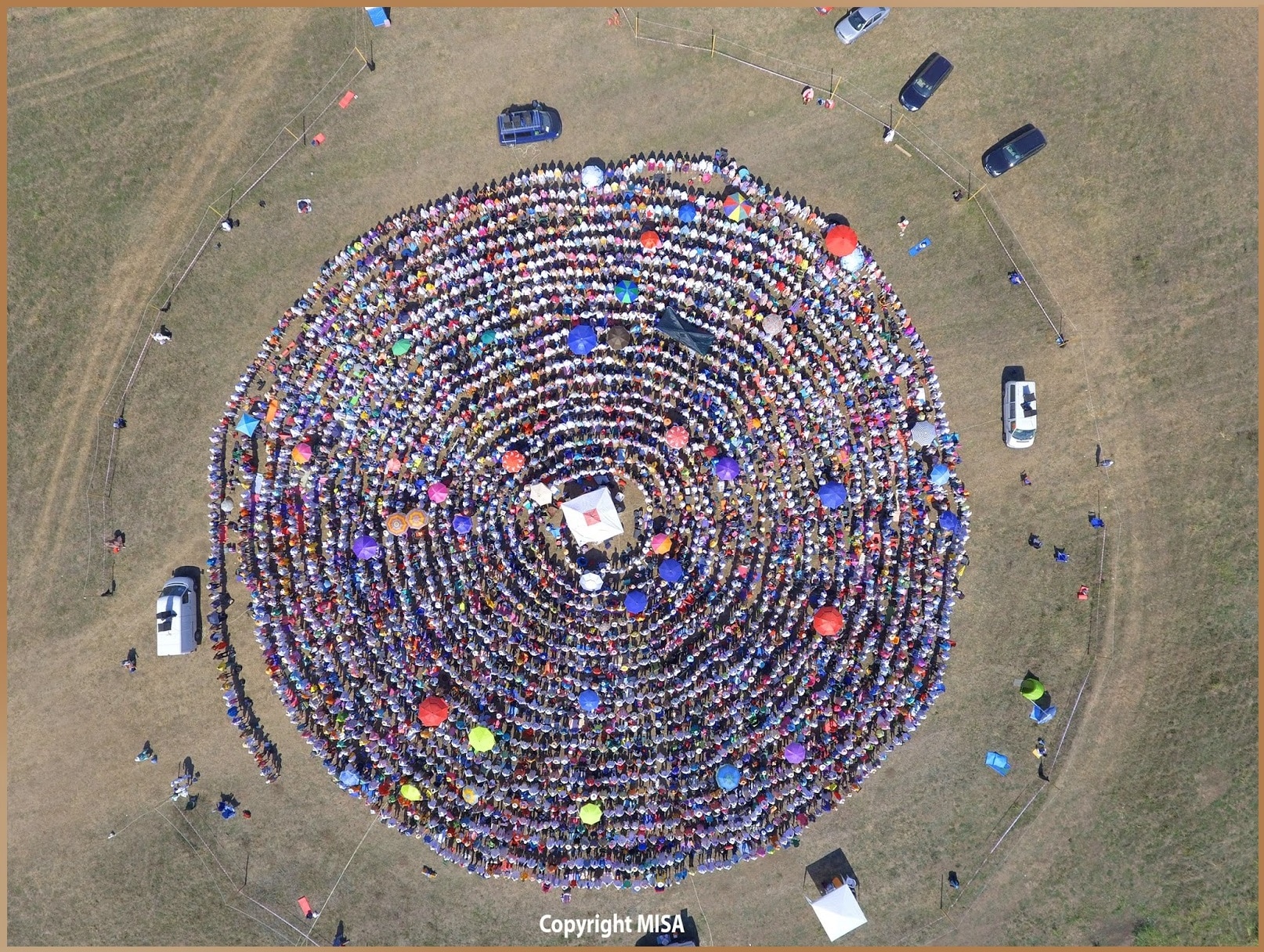 Aerial view of a large spiral formation created by participants at the MISA yoga camp in Costinești, with colorful umbrellas and mats.