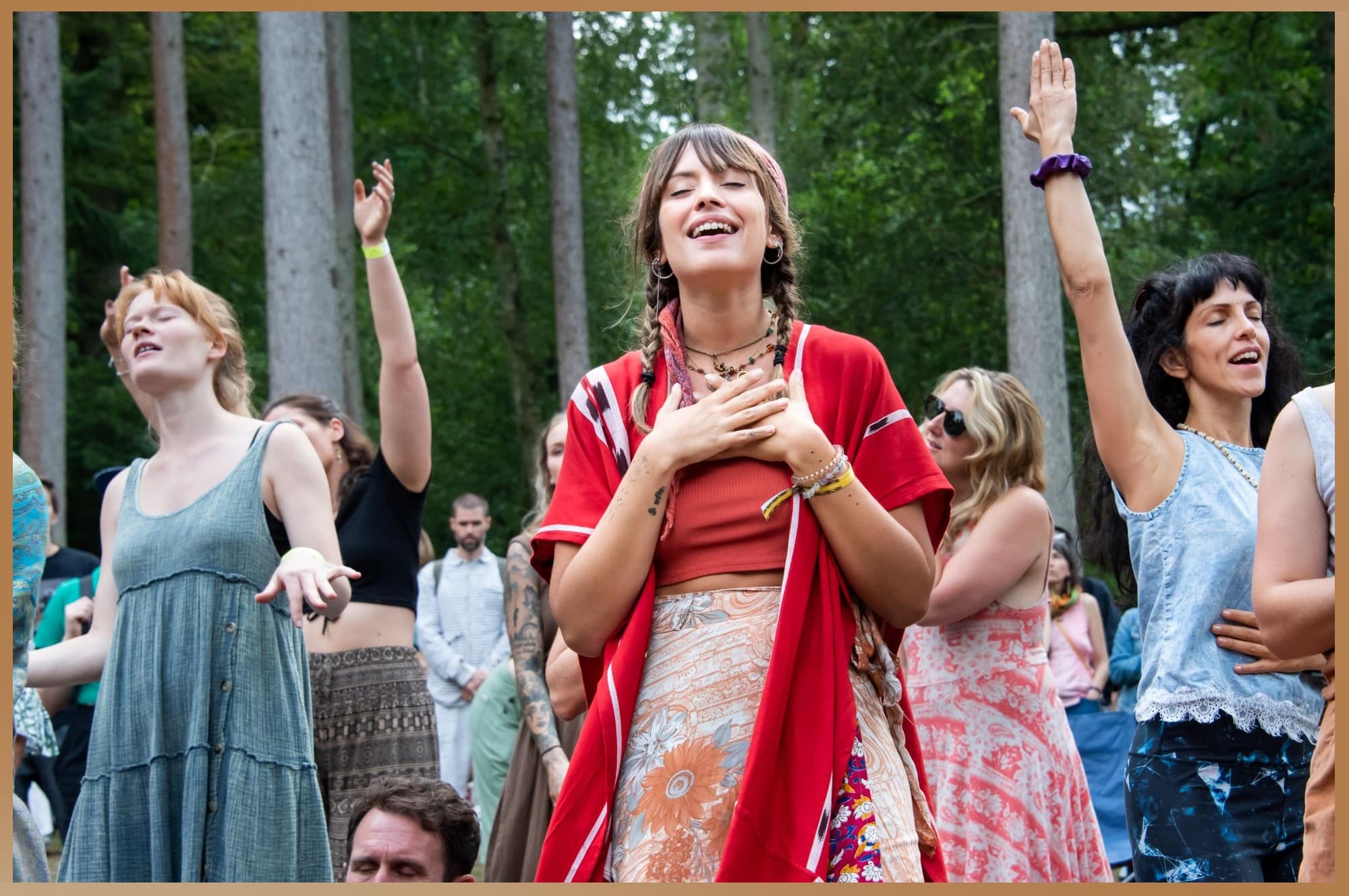 A woman joyfully dances among other participants in a forest setting at the Medicine Festival, embodying the festival's focus on personal growth and communal healing.