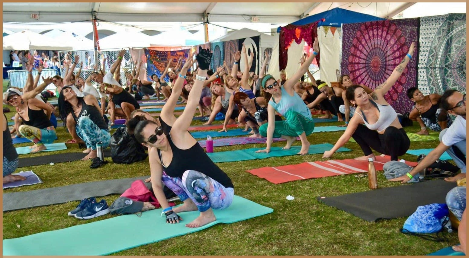 Group of participants engaging in a yoga session under a tent at The OM Festival, surrounded by colorful tapestries and vibrant atmosphere.