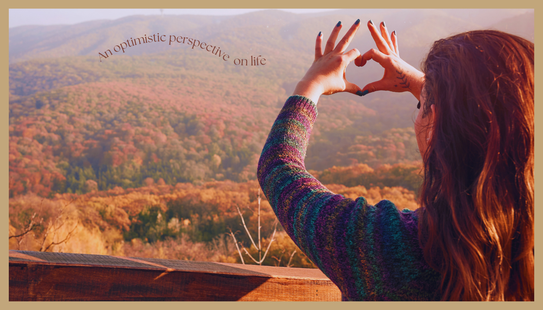 A woman forming a heart shape with her hands while overlooking colorful autumn mountains, symbolizing gratitude and an optimistic perspective on life.
